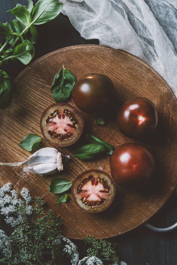 top view of black prince tomatoes, basil leaves and garlic on cutting board with gauze Pomodoro Ciliegia Brown Berry semi
